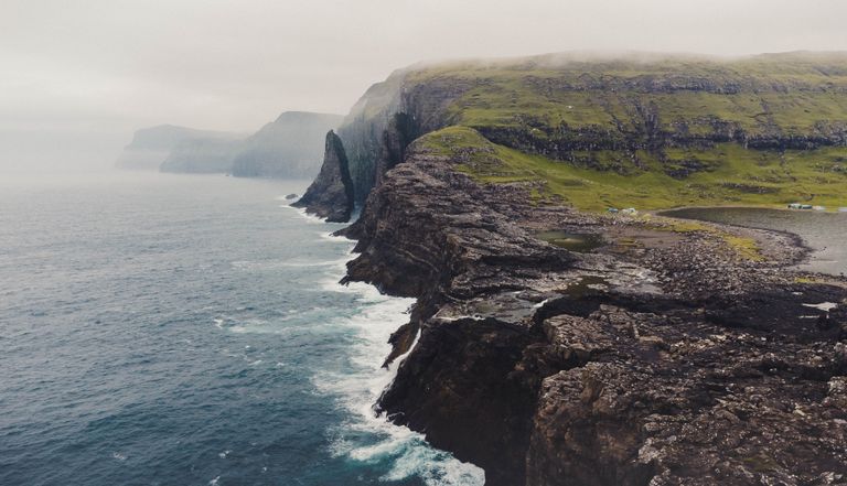 Aerial view of misty cliffs meeting the sea in Vága, Faroe Islands, capturing nature's rugged beauty.