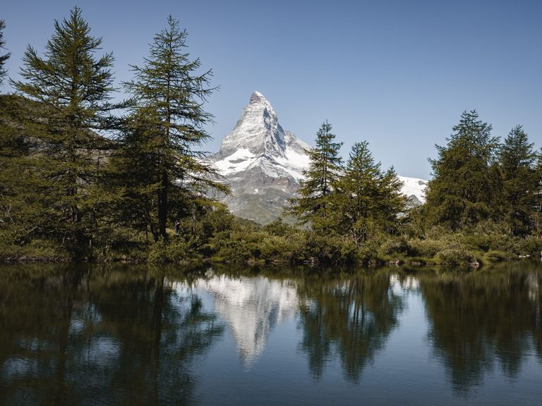 Beautiful landscape of the Matterhorn reflected in a serene alpine lake surrounded by lush greenery.
