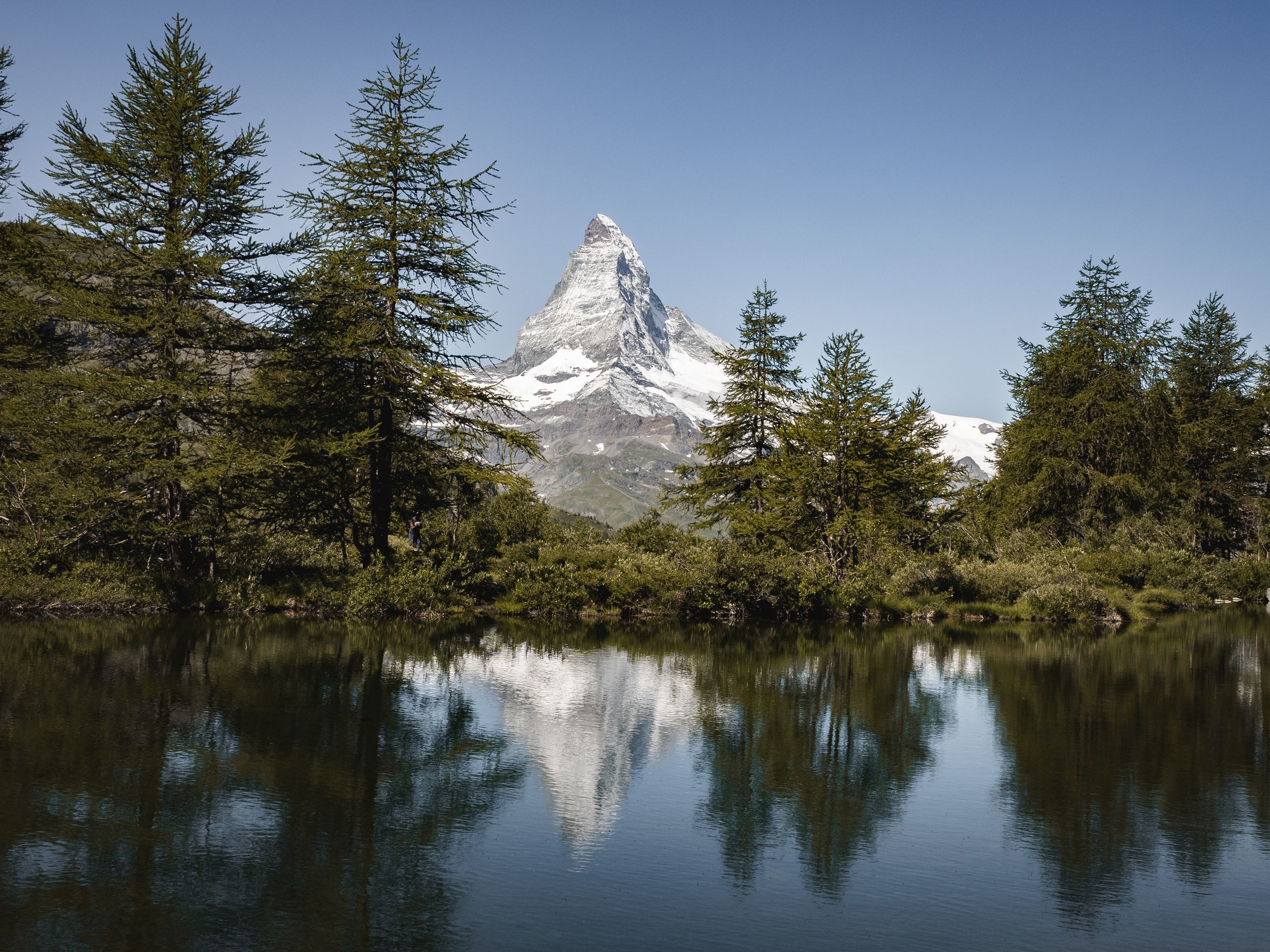 Beautiful landscape of the Matterhorn reflected in a serene alpine lake surrounded by lush greenery.