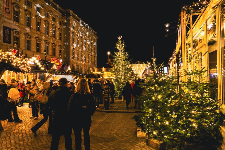 Festive night scene at a Christmas market with illuminated stalls and lively crowds.